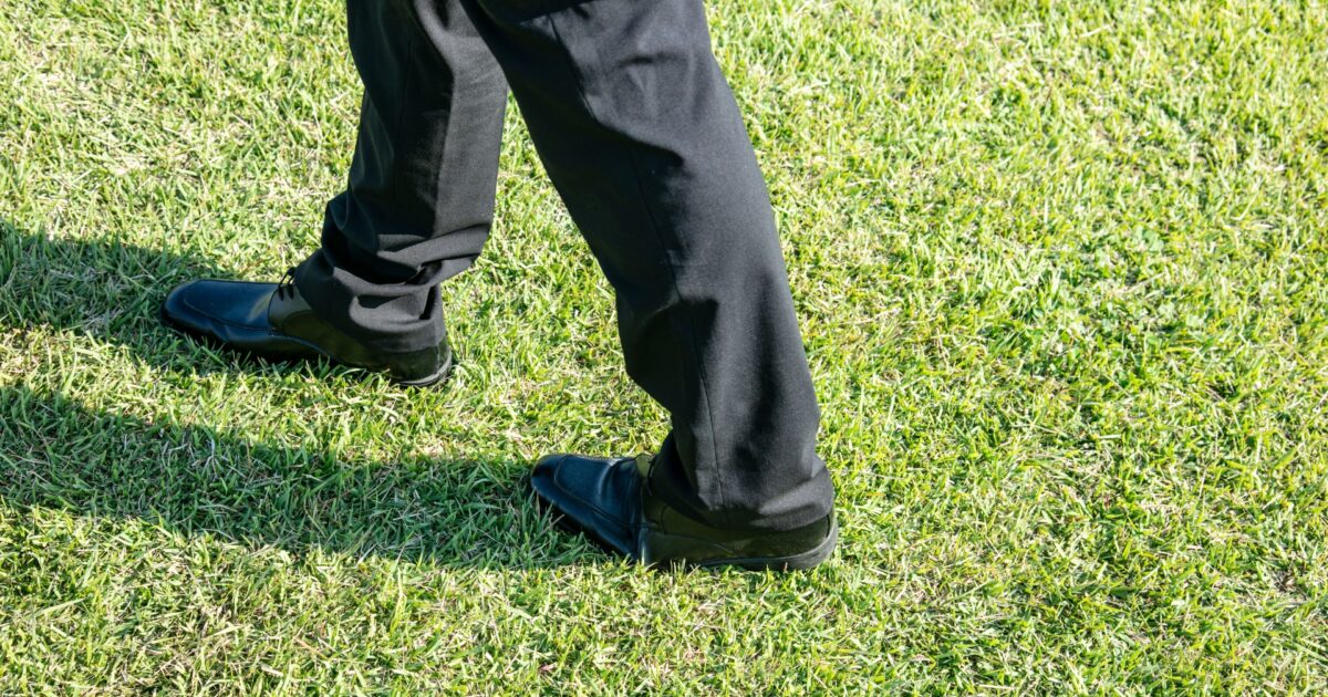 黒いスラックスと革靴で芝生を歩く男性の足元