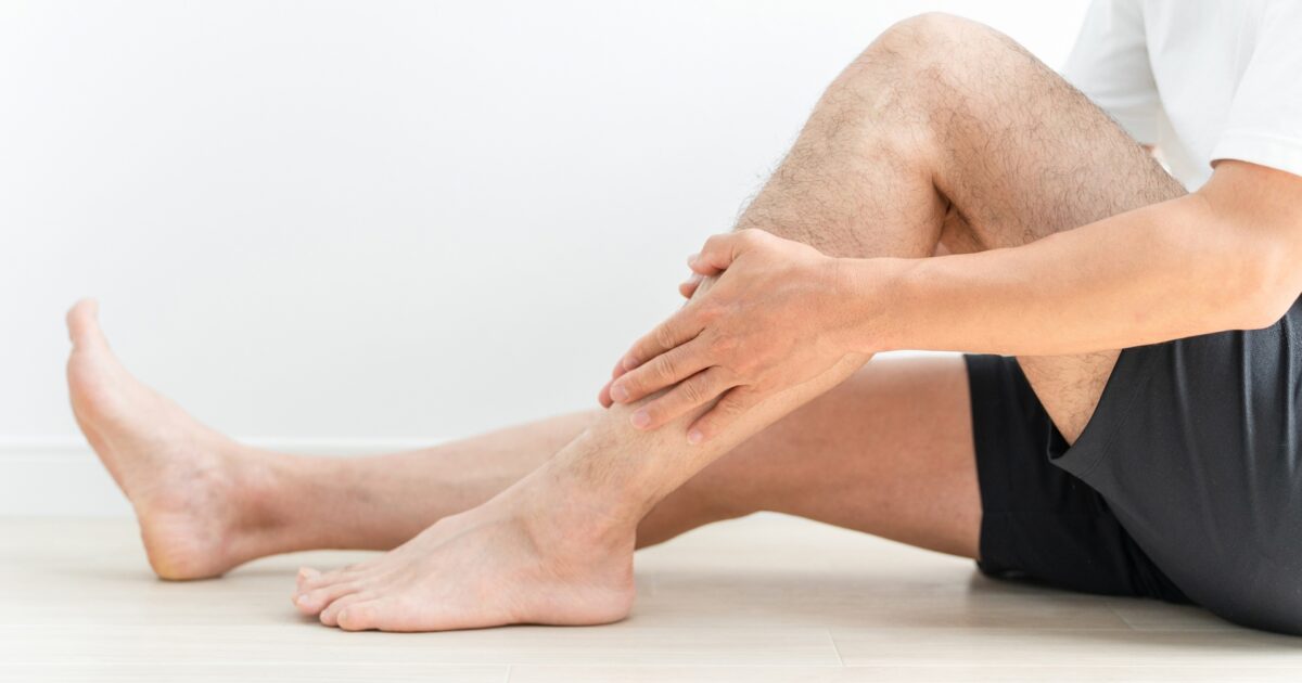 床に座りすねを両手で押さえる短パン姿の男性