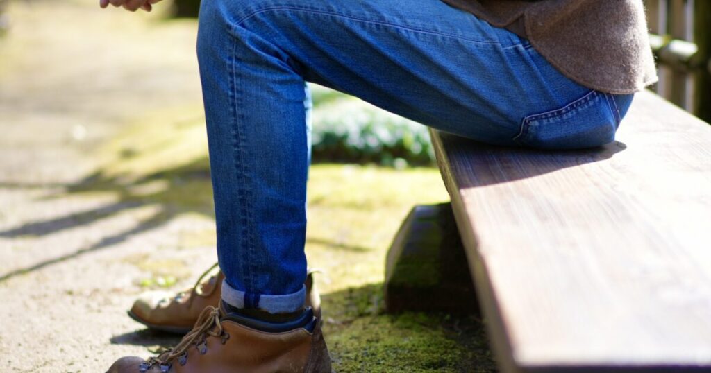 デニムと登山靴でベンチに座る男性の足元