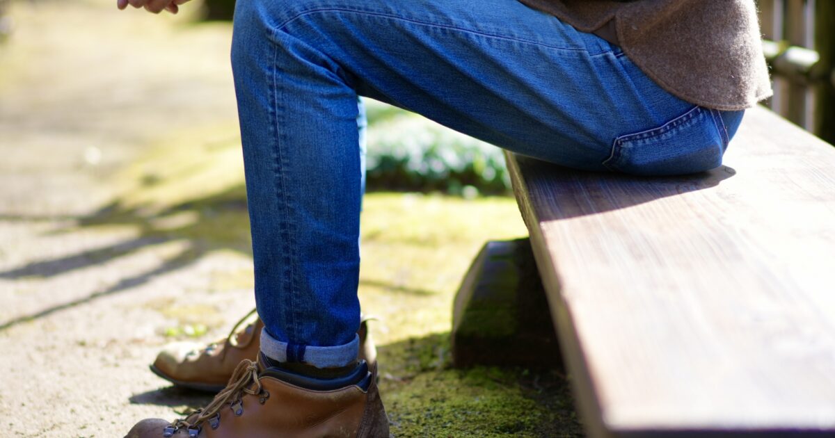 デニムと登山靴でベンチに座る男性の足元