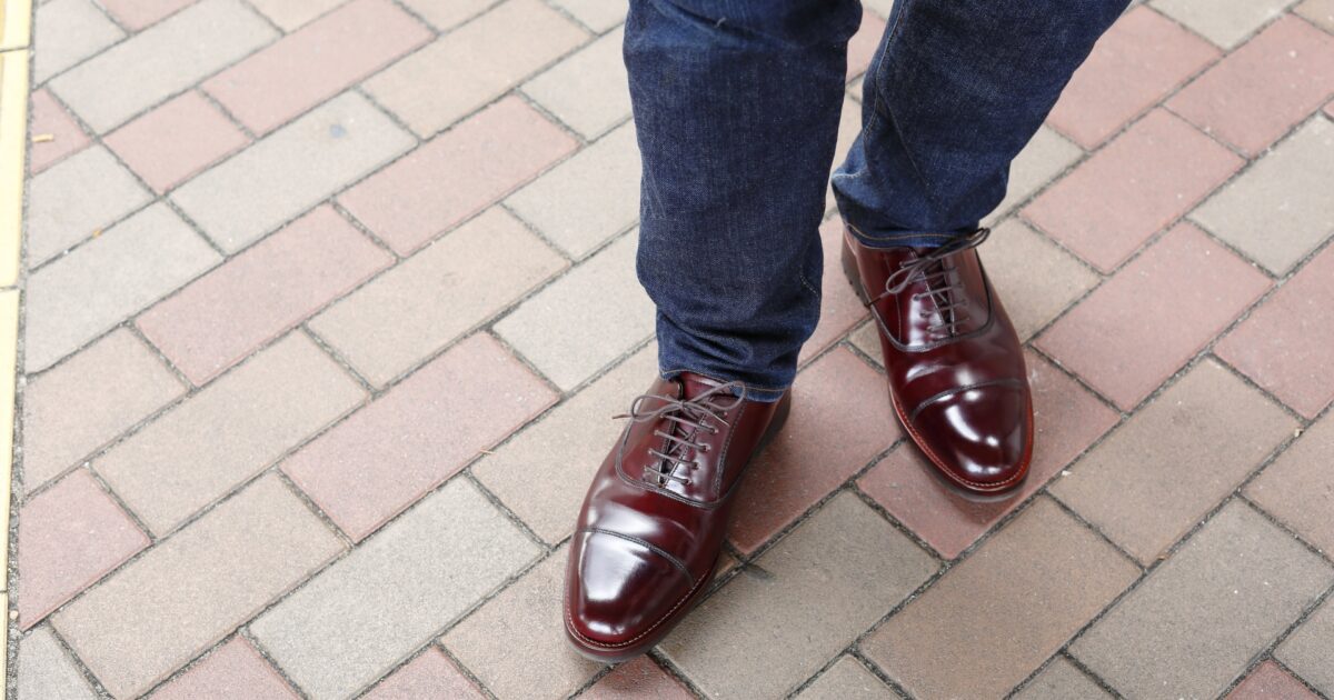 濃紺ジーンズと赤茶色の革靴を履いた男性の足元