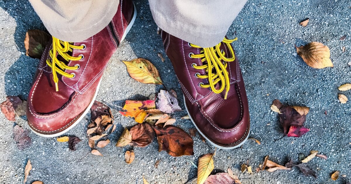 黄色い靴ひも付きの赤いレザーシューズとベージュのパンツの足元