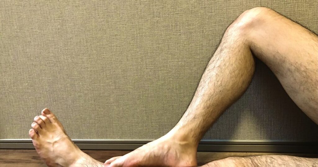 室内で壁にもたれて足を伸ばす男性の脚