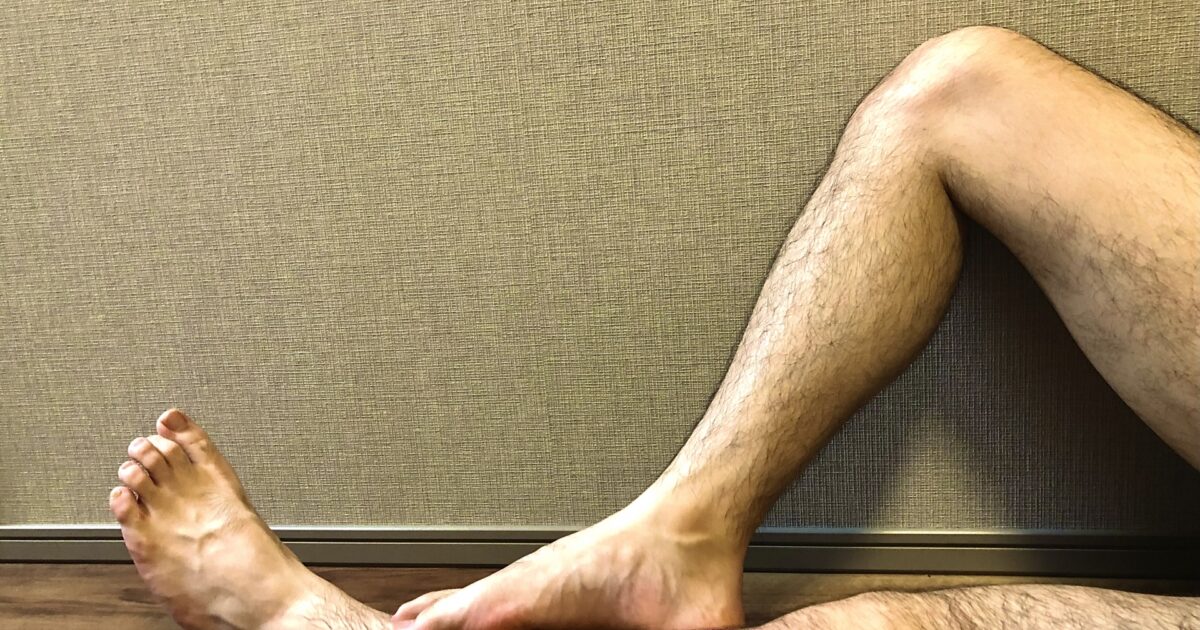 室内で壁にもたれて足を伸ばす男性の脚