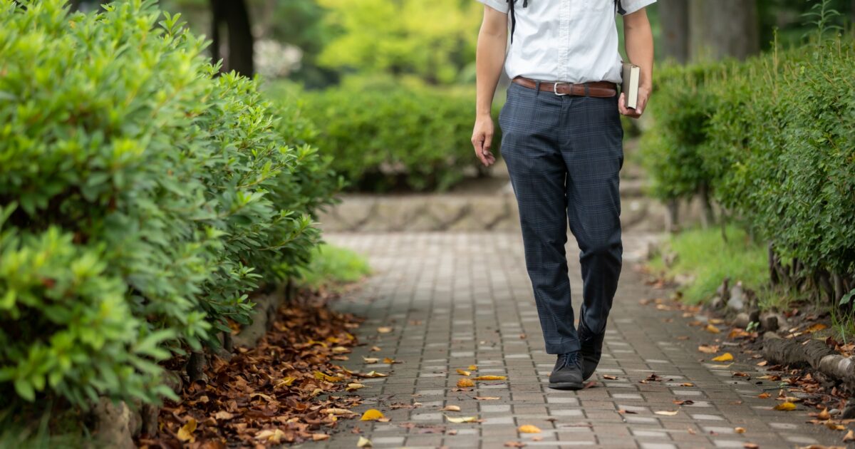 チェック柄のスラックスを履いた男性が公園の小道を歩く様子